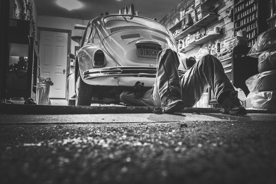 Man, lying on the concrete under his car and repairing it in the garage